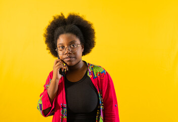 mujer afro usando gafas y su cabello recogido en un fondo de color amarillo con una mano junto a su...