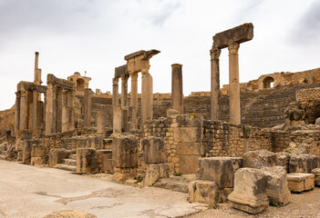 View of remains of ancient stone stage columns and seating steps of Roman theatre in Dougga against...