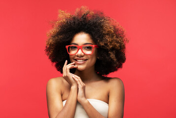 Happy Afro woman wearing eyeglasses smiling, has good mood isolated on studio red background.