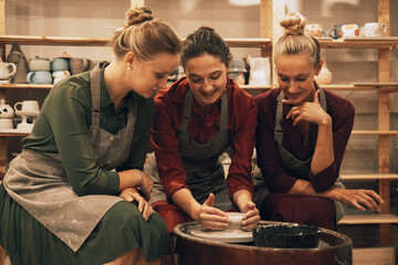 A company of three young women friends make ceramic mugs in a pottery workshop.