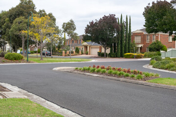 A suburban road with a T-intersection and a median nature stripe in the middle, with residential...