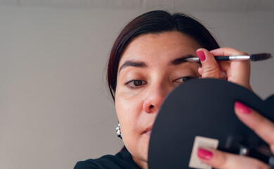 latin woman using eyebrow gel in front of a hand mirror