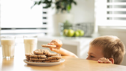 A boy is peeping at an appetizing stack of freshly baked chocolate cookies on the table.