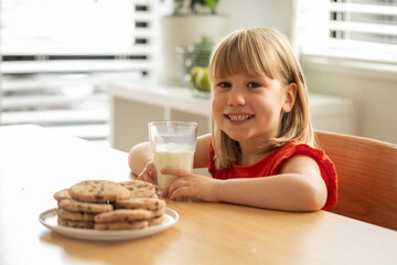 Cheerful girl enjoying fresh milk and homemade cookies, perfect for a wholesome snack time.
