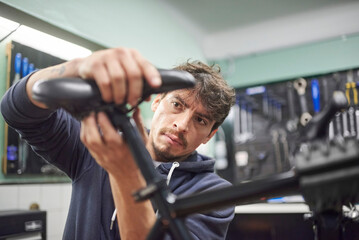 Young hispanic man assembling a bicycle saddle in his bike workshop as part of a maintenance...