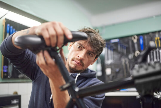 Young hispanic man assembling a bicycle saddle in his bike workshop as part of a maintenance service. Real people at work.Composition with selective focus and copy space.