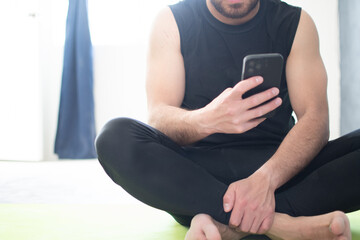 Hombre haciendo yoga en su casa y usando el teléfono celular. 