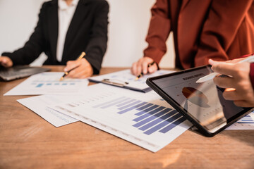 Diverse group of professionals businesswomen gather in meeting room for collaborative discussions on finance, strategy, and teamwork, technology tablets and laptops for data analysis and presentation