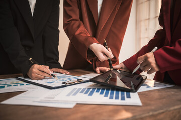 Diverse group of professionals businesswomen gather in meeting room for collaborative discussions on finance, strategy, and teamwork, technology tablets and laptops for data analysis and presentation