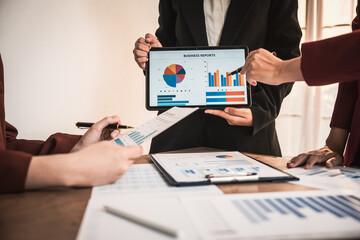 Diverse group of professionals businesswomen gather in meeting room for collaborative discussions on finance, strategy, and teamwork, technology tablets and laptops for data analysis and presentation