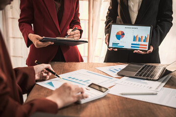 Diverse group of professionals businesswomen gather in meeting room for collaborative discussions on finance, strategy, and teamwork, technology tablets and laptops for data analysis and presentation