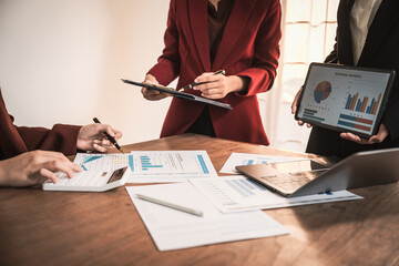 Diverse group of professionals businesswomen gather in meeting room for collaborative discussions on finance, strategy, and teamwork, technology tablets and laptops for data analysis and presentation