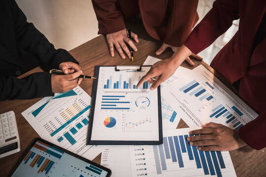 Diverse group of professionals businesswomen gather in meeting room for collaborative discussions on finance, strategy, and teamwork, technology tablets and laptops for data analysis and presentation - Powered by Adobe