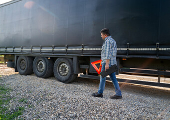 Truck driver walking by the trailer holding a warning triangle 