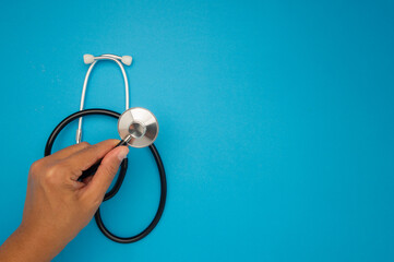 Close-up of a doctor's hand holding a stethoscope on a blue background.