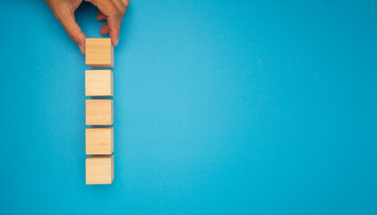 A hand is arranging wooden blocks in a vertical line on a vibrant blue background.