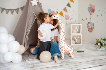 Curly mother and daughter playing in children's room with toys and tent
