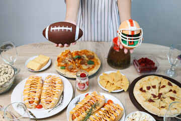 Hand Showing Rugby Ball and Helmet Above Assorted Food to Watch Super Bowl Match 