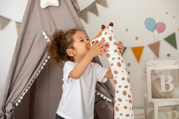 Little happy child girl 4-6 years old wearing casual clothes, having fun, hugging toy giraffe...