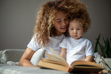 Curly mother and daughter in white T-shirts reading a book