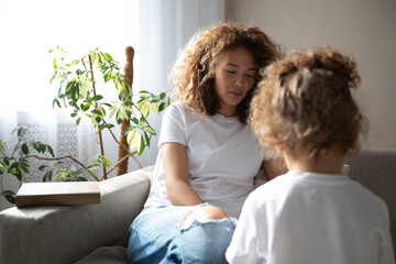 Curly mother and daughter in white T-shirts reading a book