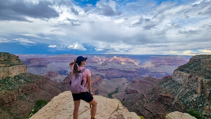 Rear view of woman with hiking backpack standing in a rock on Bright Angel trail with panoramic aerial overlook of South Rim of Grand Canyon National Park, Arizona, USA, America. Amazing vistas