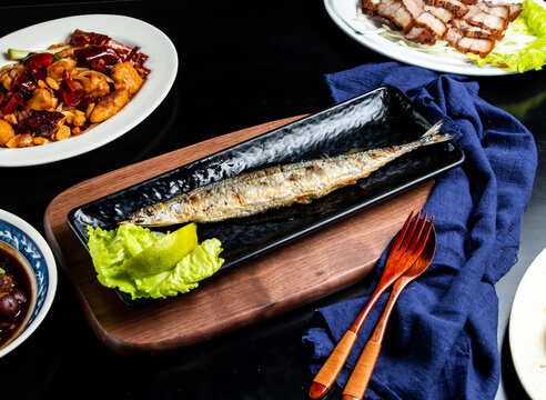 Grilled saury fish with lemon and lettuce spoon and fork served in dish isolated on wooden board side view of taiwan food