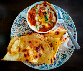 Tandoori roti with a bowl of curry in plate kept on a table.
