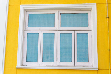 Fototapeta premium A White Wooden Window on a Yellow Wall: Square Italian Architecture Background with Vibrant Color Yellow Wall Facade. Small Town House Exterior