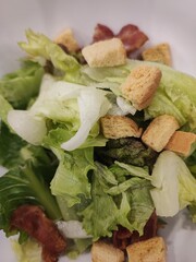 Caesar salad with fresh vegetables, ham, and bread placed on a plate