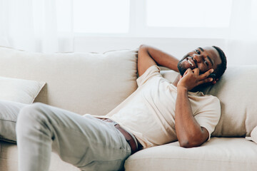 Relaxing Chat on the Black Sofa African American Man Holding a Smartphone for a Happy Video Call in...