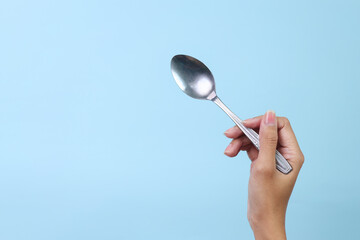 Woman's hand holds a stainless spoon on a blue pastel background.