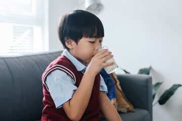 Healthy schoolboy in uniform drinking glass of milk for breakfast before go to school.