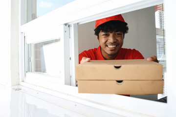 Young worker in red uniform serving two boxes of pizza for customer to take away.