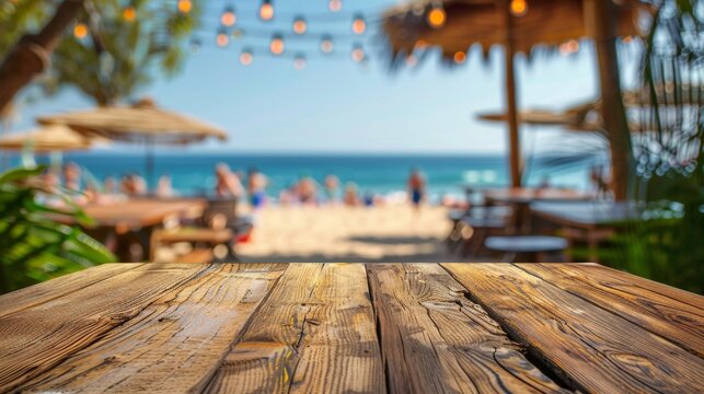 An empty wooden table with a blurred beach party in the background, setting the stage for summer gatherings.