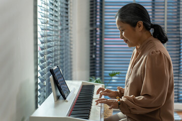 Asian attractive senior mature woman play piano in living room at home. 