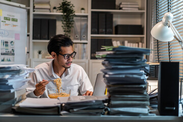 Asian young businessman eating noodles while working in office at night.