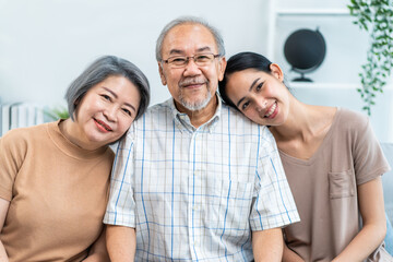 Portrait of Asian senior couple sitting on sofa with daughter in house. 