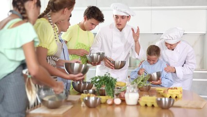 During cooking lesson, female cook tells children about culinary rules, guy assistant helps child . High quality 4k footage