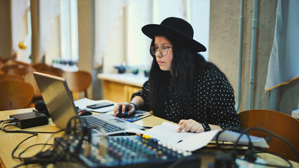 A schoolgirl wearing a hat at a mixing console and computer before an event.
