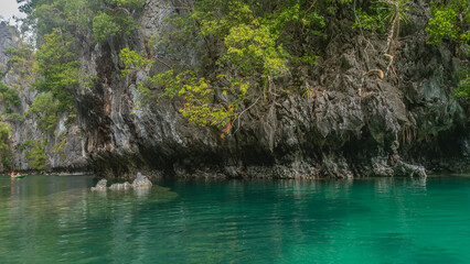 Picturesque steep karst cliffs surround the emerald Bay. Green tropical vegetation on steep limestone slopes. A canoe with tourists floats on clear water. Philippines. Small lagoon. Bacuit Bay.Palawan