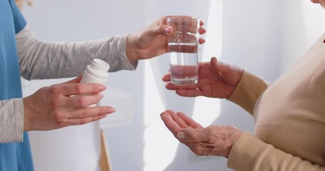 Close up shot of a hands of a doctor or nurse give pills and a glass of water to a senior patient. Conveying the importance of healthcare support and proper medication intake in the treatment process.