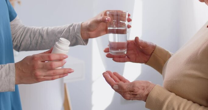 Close up shot of a hands of a doctor or nurse give pills and a glass of water to a senior patient. Conveying the importance of healthcare support and proper medication intake in the treatment process.
