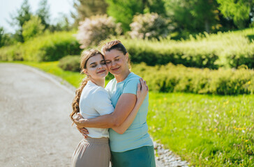 Mother and daughter embracing in park, content, sunny.