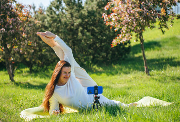 Woman doing yoga in park, stretching, recording video.