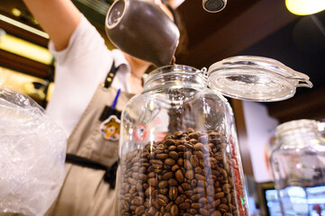 Close-up of a barista's hand refilling a coffee grinder with fresh beans from a jar