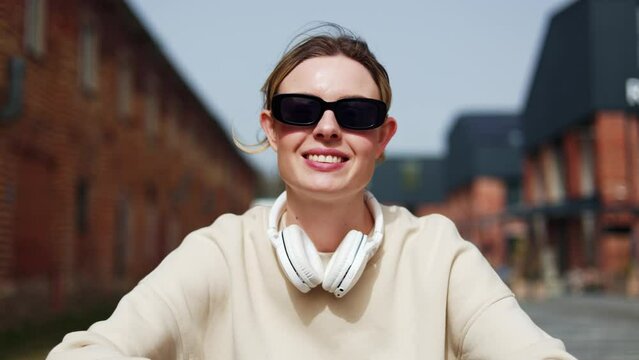 First person view of happy woman wearing dark glasses talking with enthusiasm and looking at camera. Adorable female speaking and nodding head during online video call while sitting in public place.