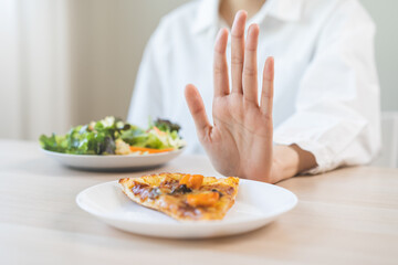 Diet concept, asian young woman close up hand push out away Pizza, refuse junk process, carb food on plate, choose green vegetable salad, eat low fat for good health. Female people getting weight loss