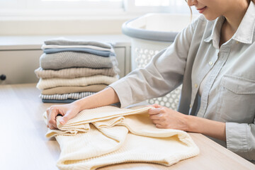 Housewife working asian young woman, girl hand in many folding freshly white sweaters or dressing...