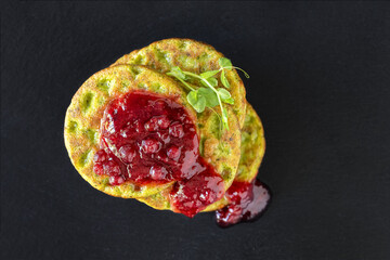 Spinach pancakes with berry jam on the black background, view from top